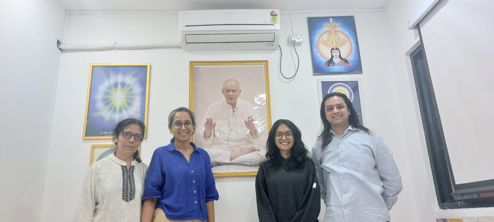 A group standing together inside the center, with framed healing charts and a portrait of Grand Master Choa Kok Sui on the wall behind them